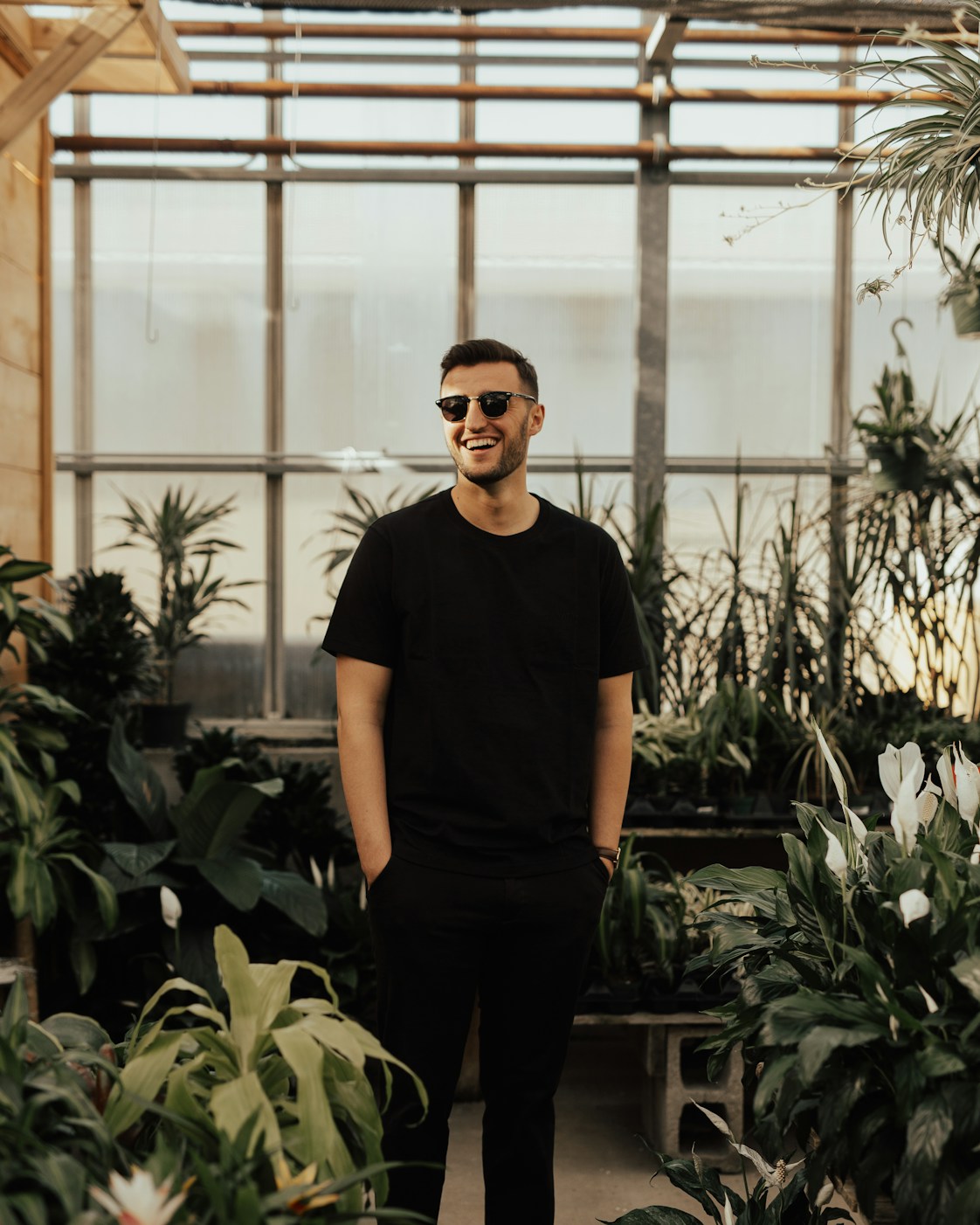 A smiling man standing among rows of green plants in a bright greenhouse
